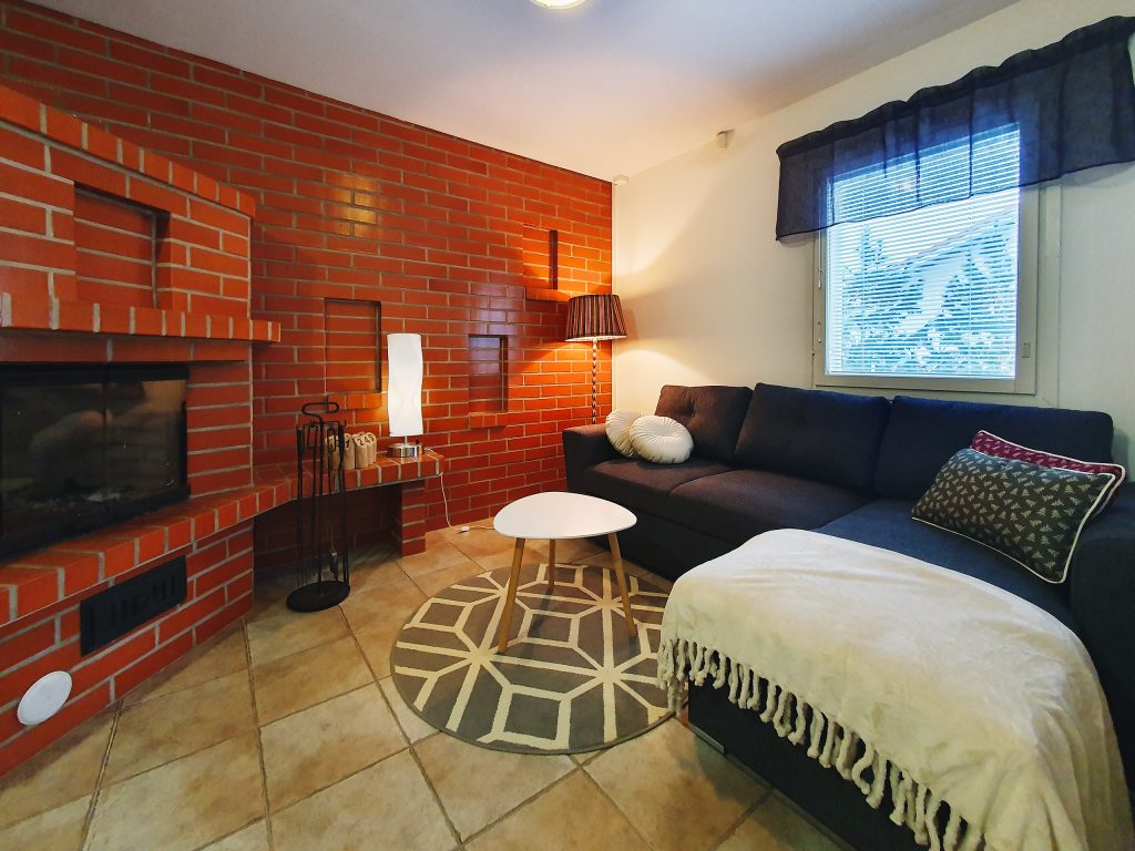 Omakotitalon tilava takkahuone suurella punatiilisellä takalla ja sohvalla.