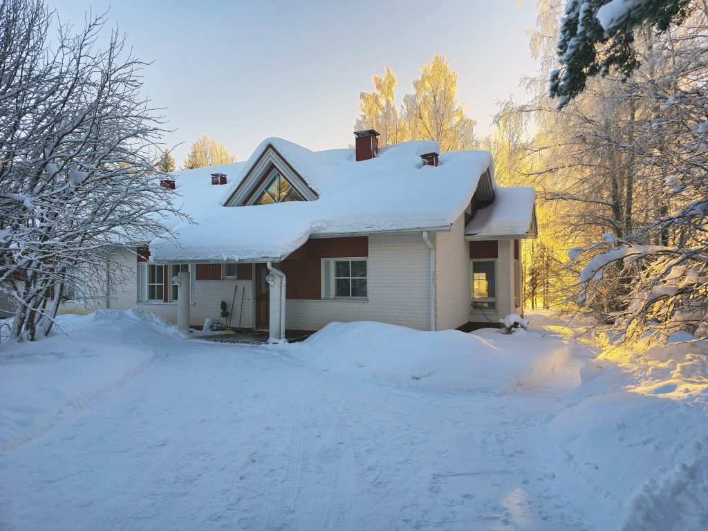 Valkotiilinen omakotitalo kylpee kultaisessa auringonpaisteessa Rovaniemen lumisessa kevättalvessa.